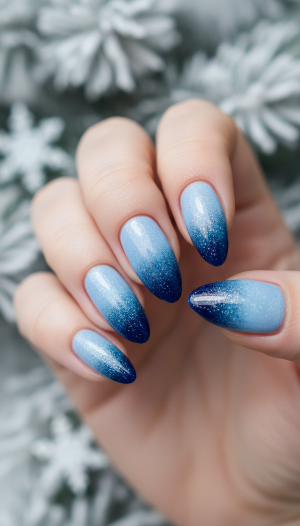 A close-up view of elegant gradient icy nails, showcasing a stunning transition from pale blue at the cuticles to deep navy at the tips, reflecting a shimmering, frosty finish. The nails are neatly manicured, extending gracefully against a softly blurred winter background of frosted pine branches. Soft, diffused lighting casts a gentle glow, emphasizing the cold, crystalline texture of the nail polish while creating a serene and sophisticated atmosphere. The shot is captured with a macro lens to focus on the intricate details of the nail art, emphasizing the smooth gradients and ice-like sparkle. The overall mood is wintry and elegant, perfectly capturing the essence of icy nail designs.